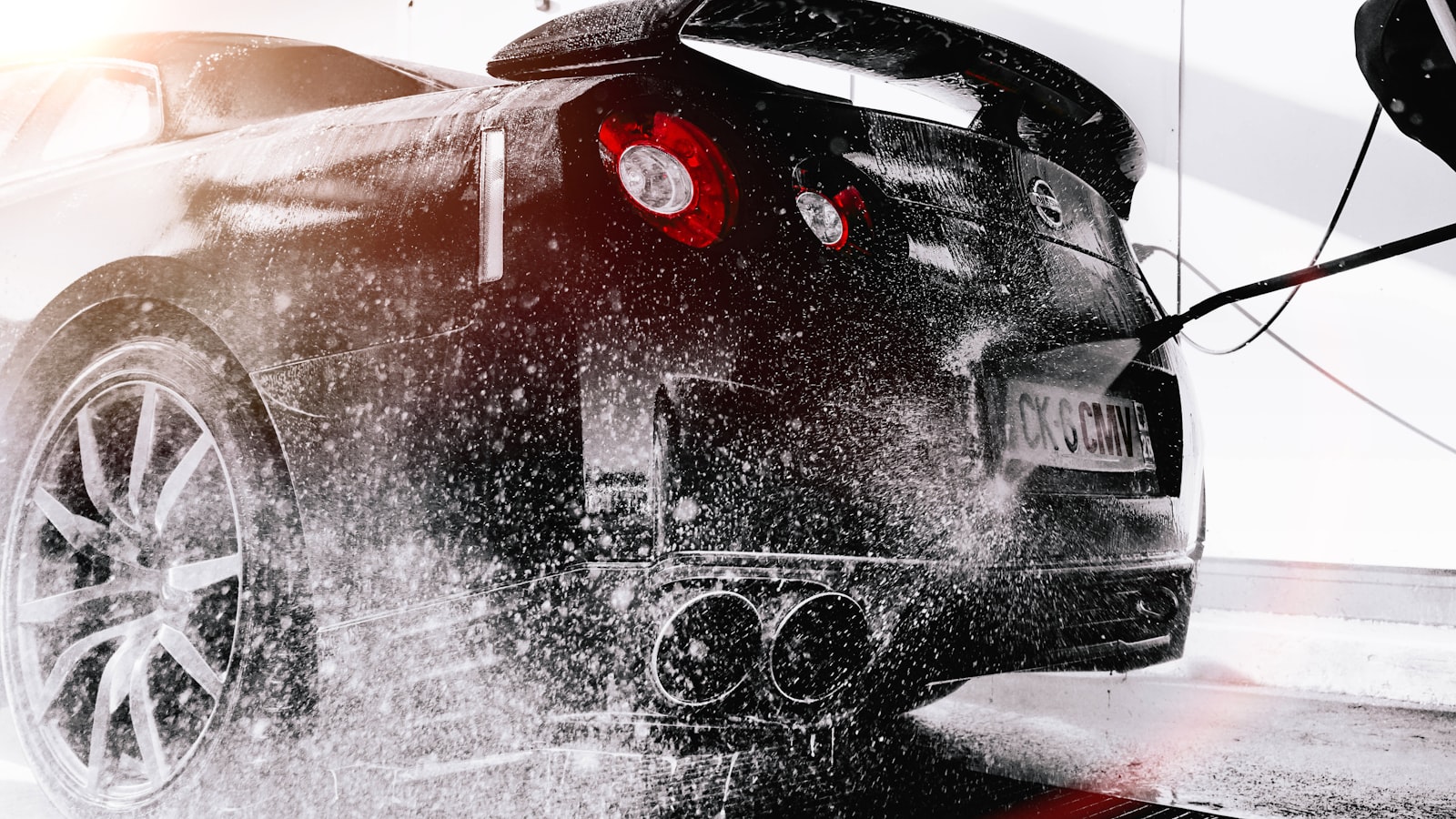 A dark sports car being rinsed under a high-pressure spray during a detail.