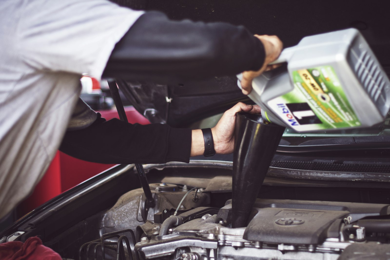A mechanic pouring fresh oil into an engine through a funnel.